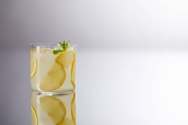 один стакан свежего лимонада на отражающей поверхности и на сером
