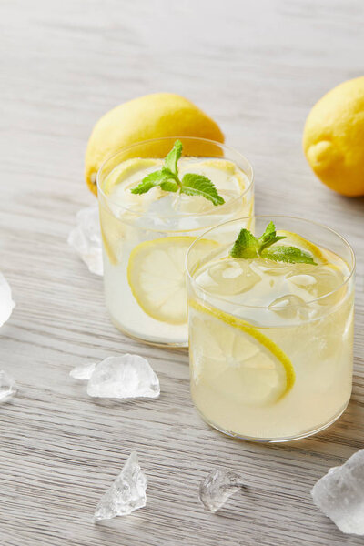 стаканы вкусного лимонада со льдом и лимонами на деревянной поверхности

