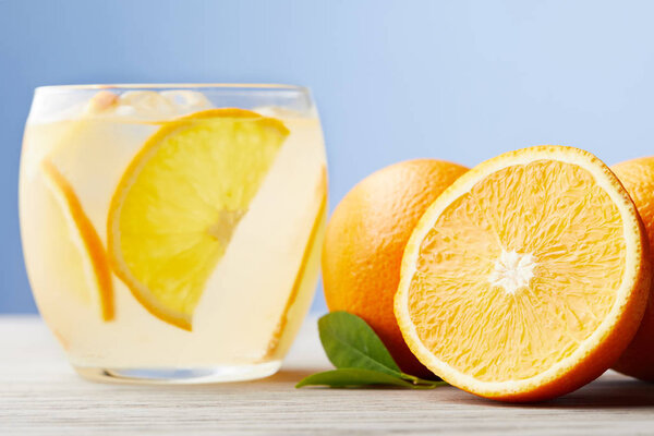 glass of fresh lemonade with ripe oranges on wooden table