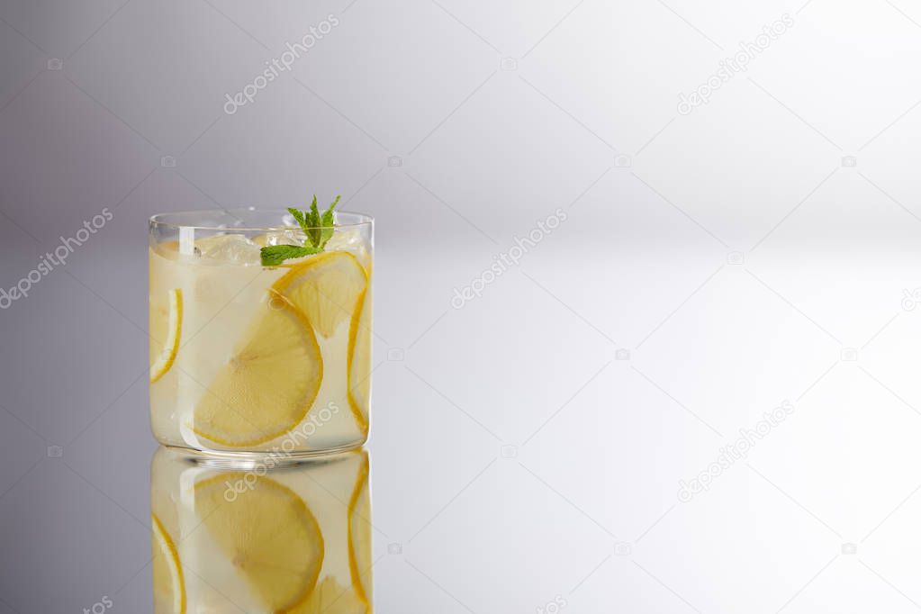 single glass of fresh lemonade on reflective surface and on grey