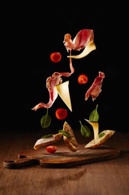 Ingredients for snack with bread, jamon and vegetables flying above wooden table surface clipart