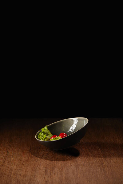Ripe tomatoes and salad leaves in bowl on wooden table 