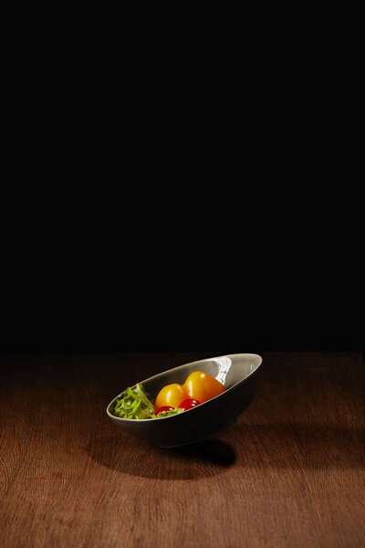 Bowl with tomatoes and salad leaves on wooden table 