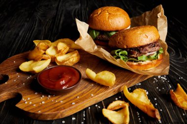 Tempting fast food diner with burgers and potatoes with sauce on cutting board