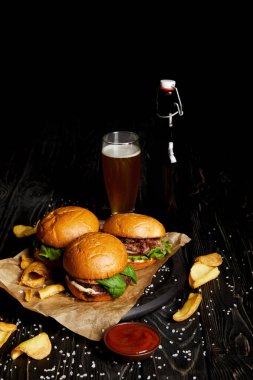 Hamburgers and french fries on table with beer in bottle and glass clipart