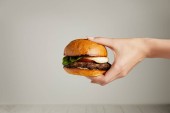 Teplé chutné burger v ženské ruce na šedém pozadí
