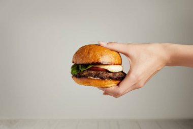 Hot tasty burger in female hand on grey background