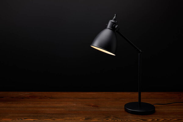 close up view of black lamp on wooden tabletop on black background