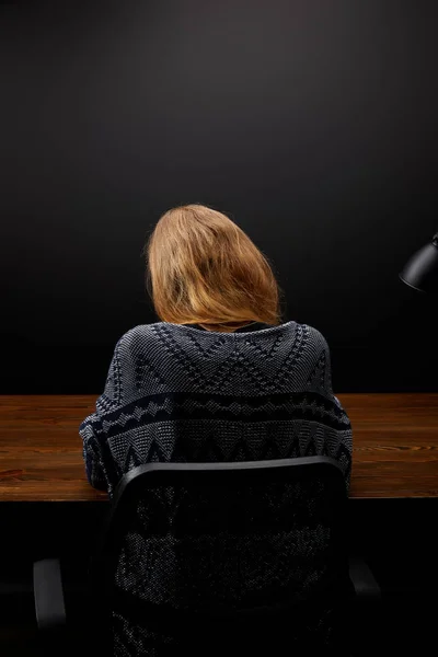 back view of woman sitting at wooden tabletop with black wall backdrop