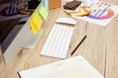 close up view of designer workplace with computer screen with colorful stickers, notebooks and pallet on wooden tabletop clipart