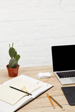 grafik tasarımcı işyerinde ahşap yüzey üzerinde laptop, grafik tablet ve boş defter görünümü kadar kapatın