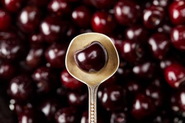 top view of fresh ripe sweet cherry on vintage spoon on blurred cherries background clipart