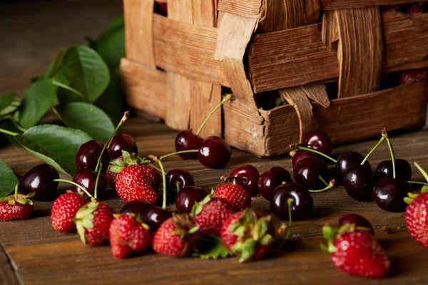 ripe cherries and strawberries on wooden surface with leaves and rustic box