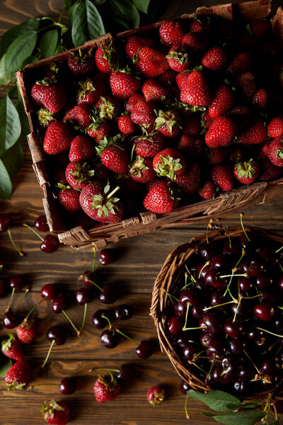 top view of cherries and strawberries in basket and box on wooden surface