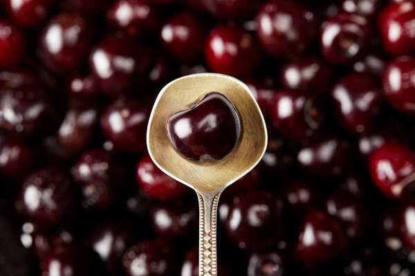 top view of fresh ripe sweet cherry on vintage spoon on blurred cherries background