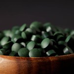 Vue rapprochée de bol en bois avec pile de pilules de spiruline isolé sur fond gris