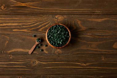 ahşap masa üstünde tahta kaşık ve spirulina hapları yığını ile kase üstten görünüm