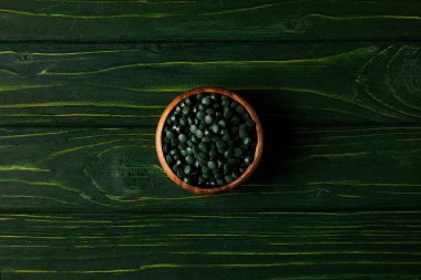 spirulina hapları yığını ile ahşap kase üstten görünüm yeşil ahşap tablo