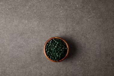 top view of wooden bowl with pile of spirulina pills on stone table  clipart