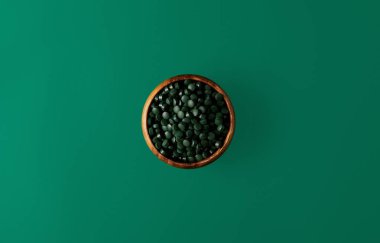 ahşap kase yeşil izole spirulina hapları yığını ile üstten görünüm  