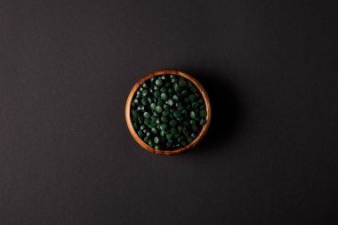 top view of wooden bowl with pile of spirulina pills on grey table  clipart