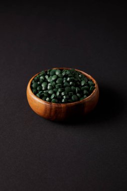 wooden bowl with pile of spirulina pills on grey table  clipart