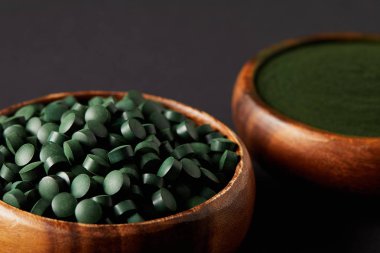 close up view of wooden bowls with ground spirulina and spirulina in pills on grey background   clipart