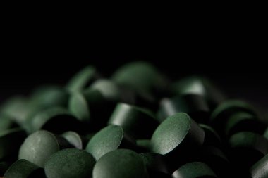 selective focus of pile of spirulina pills isolated on black background  clipart