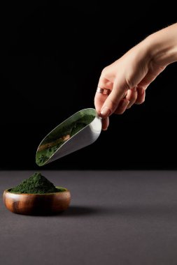 spirulina tozu kepçe tarafından siyah arka plan üzerine ahşap kaseye atma Kadın resim kırpılmış 