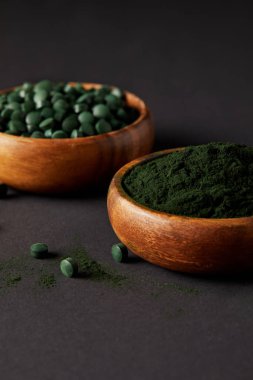 close up view of wooden bowls with ground spirulina and spirulina in pills on grey table  clipart