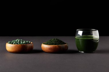 spirulina güler yüzlü, spirulina tozu ve siyah arka plan üzerine spirulina hapları ile kase cam