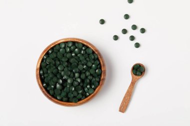 elevated view of wooden spoon and bowl with pile of spirulina pills on grey table  clipart