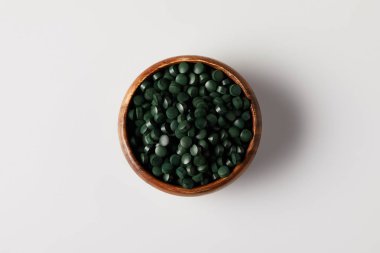 top view of wooden bowl with pile of spirulina pills on grey table clipart