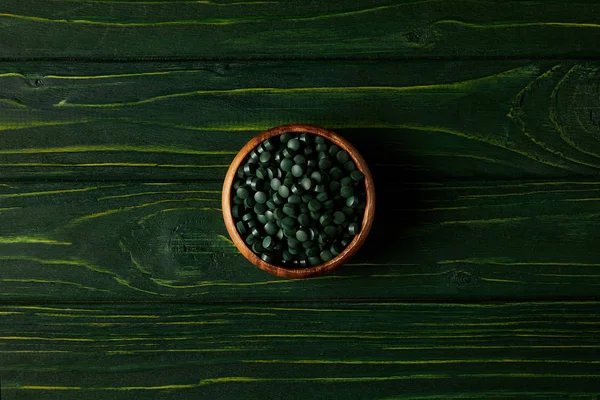 Ovanifrån Träskål Med Högen Spirulina Tabletter Gröna Träbord — Gratis stockfoto