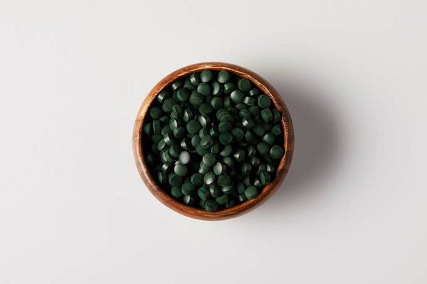 top view of wooden bowl with pile of spirulina pills on grey table
