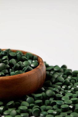 close up view of wooden bowl and pile of spirulina pills isolated on grey background  clipart