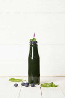 seçici odak spirulina güler yüzlü nane ile şişe yaprakları, yaban mersini ve saman üzerinde ahşap masa içme 