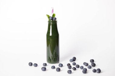 spirulina yüzlü yaprakları ve beyaz arka plan üzerinde yaban mersini çevrili içki bardağı taşıran damla ile şişe