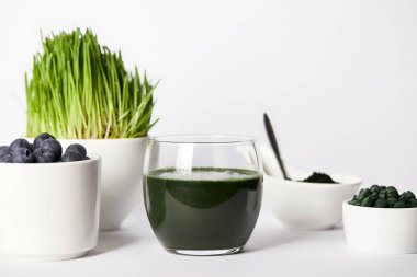 Spirulina güler yüzlü, kaşık, bardak spirulina çim ve yaban mersini, kaseler spirulina tozu ve spirulina hapları gri arka plan üzerinde 