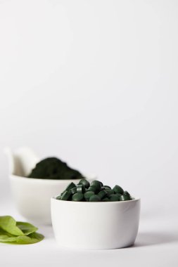 selective focus of leaves, bowls with spirulina pills and spirulina powder on grey background  clipart