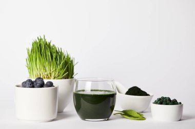 fresh smoothie from spirulina, cups with spirulina grass and blueberries, leaves, bowls with spirulina powder and spirulina pills on grey background  clipart