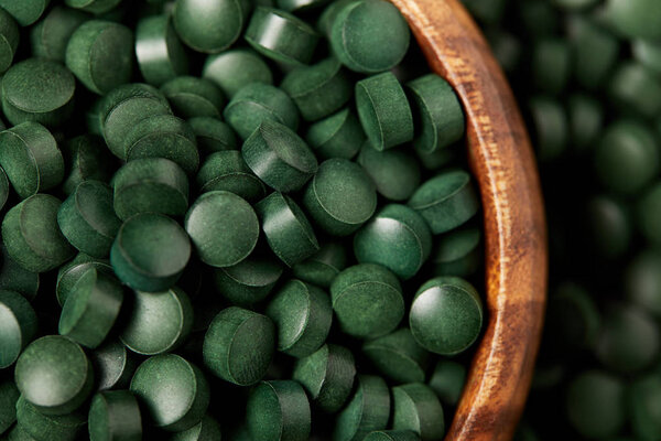 close up view of wooden bowl with pile of spirulina pills 