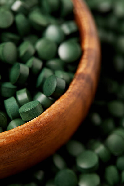 selective focus of wooden bowl with pile of spirulina pills 