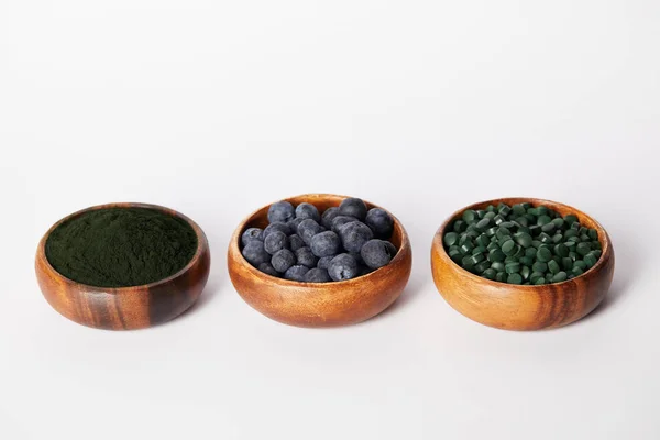 Dispostos Tigelas Madeira Com Mirtilos Pílulas Spirulina Espirulina Fundo Branco — Fotografia de Stock