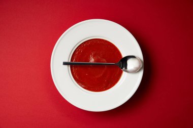 top view of tomato soup in plate and spoon on red table clipart