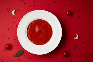 top view of tasty tomato soup and scattered pepper and tomatoes on red table clipart