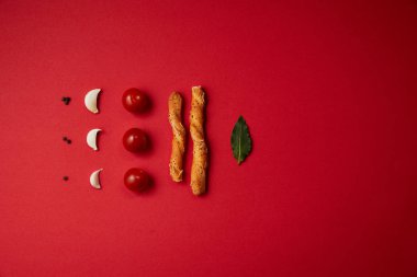 food styling of tasty tomatoes, garlic, bread sticks and bay leaf on red table clipart