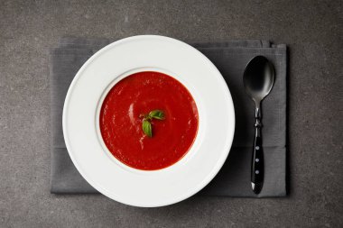elevated view of tasty tomato soup in plate and spoon on grey napkin on grey table clipart
