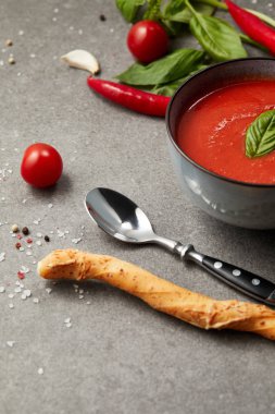 bread stick and spoon near plate with tomato soup on grey table clipart