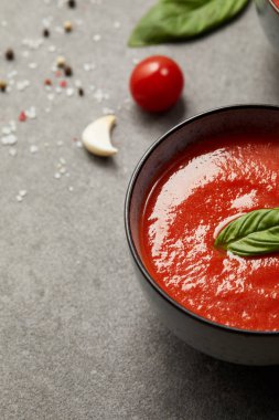 cooked tomato soup with basil in plates and tomato with garlic on grey table clipart